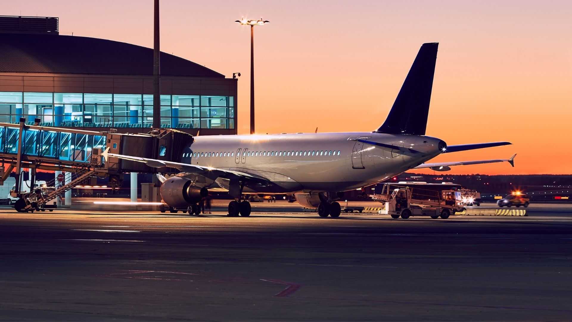 Avion de ligne commercial connecté à une passerelle de terminal VIP au coucher du soleil après l'arrivée d'un vol affrété en groupe.